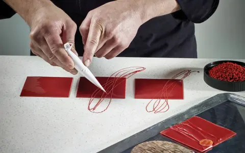 Mains travaillant avec du chocolat plastique rouge pour décorer des carrés de glaçage.