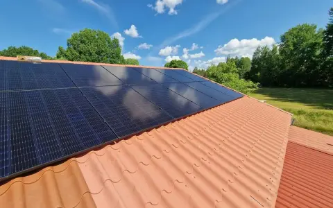 Solceller på ett tegeltak, redo för besiktning. Solen skiner på de mörka panelerna mot en blå himmel med vita moln.