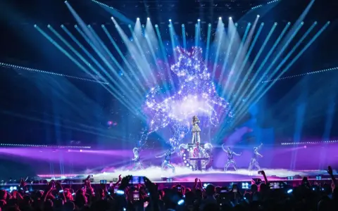 Wokalistka na scenie Eurowizji, otoczona tancerzami i efektami świetlnymi. Widownia filmuje występ, zastanawiając się, ile krajów w finale Eurowizji.