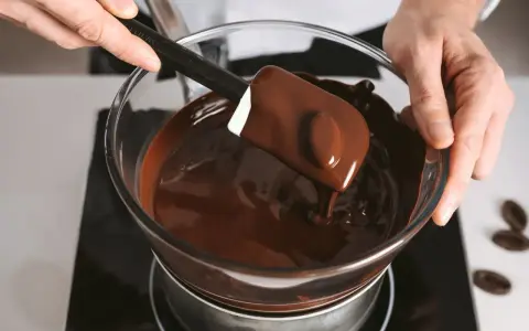 Un chocolat qui ne fond pas ? Ce n'est pas le cas ici ! Une spatule mélange du chocolat fondu brillant dans un bol en verre au-dessus d'un bain-marie.