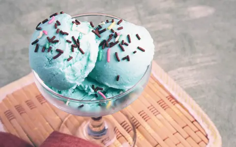 Ein Glas mit blauem Smurf-Eis, bestreut mit bunten Streuseln, steht auf einem Holzuntersetzer.