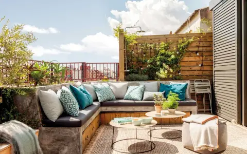 Cómodo rincón de terraza con sofás de obra, cojines turquesas y plantas. Ideas para jardineras exteriores que inspiran relax.