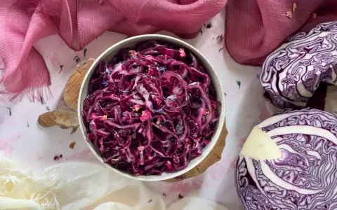 Insalata di cavolo cappuccio rosso, condita con petali di fiori, accanto a un cavolo cappuccio rosso tagliato a metà.