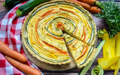 Eine bunte, vegetarische Quiche mit Zucchini und Karotten, kunstvoll im Kreis arrangiert. Frisch und lecker!