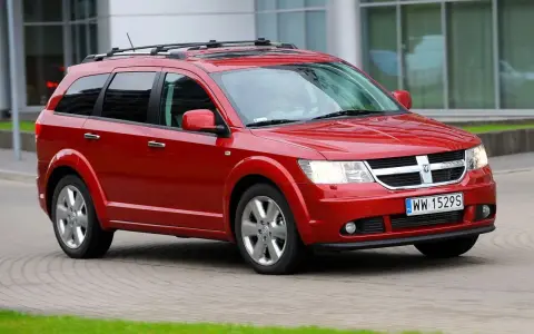 Czerwony Dodge Journey 3.6 z bagażnikiem dachowym jedzie po brukowanej drodze.