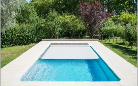 Piscina con cubierta automática, lista para reformar y disfrutar del verano. Rodeada de vegetación exuberante.