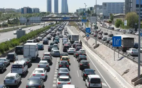 Congestión vehicular en una autopista, reflejo de la movilidad urbana. Coches y camiones detenidos en múltiples carriles bajo un cielo despejado.