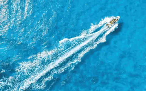 La coque d'un bateau fend les eaux bleues, laissant une traînée blanche de mousse.