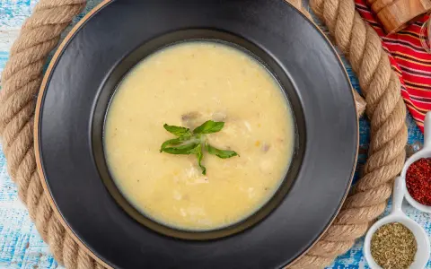 Un plato de sopa de pescado cremoso y caliente, decorado con hojas verdes, sobre un fondo rústico.