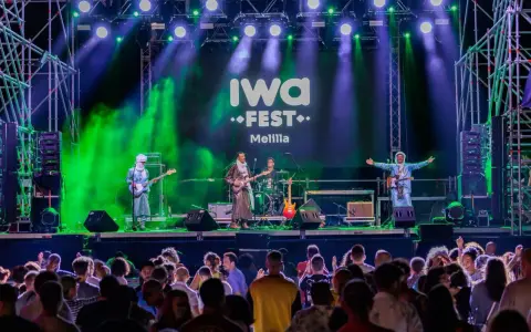 Banda tocando en el iwa fest de Melilla, con luces verdes y moradas, y una multitud disfrutando.