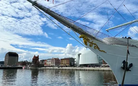 Die Gorch Fock in Stralsund, ein stolzes Segelschiff, liegt vor einer malerischen Kulisse mit historischen Gebäuden und moderner Architektur am Hafen.