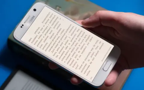 Dłoń trzyma smartfon, na którym wyświetlona jest książka do czytania na telefonie.