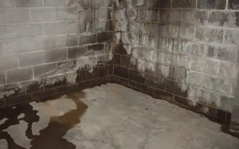 Water stains and pooling on a concrete floor and cinder block walls indicate a serious moisture problem. Learn how to get rid of moisture in basement effectively.