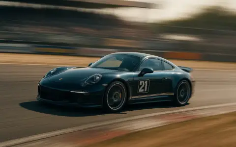 Une Porsche 911 noire, numéro 21, file sur un circuit. Le mouvement est capturé par un photo filé, créant un flou artistique autour de la voiture.