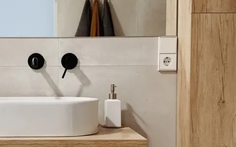 Évier moderne avec robinetterie noire, distributeur de savon et prise électrique. Un détail de la sécurité de la salle de bain.