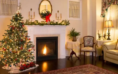 Ideas para decorar una chimenea navideña: árbol iluminado, guirnaldas verdes, un tren de juguete y un fuego acogedor.
