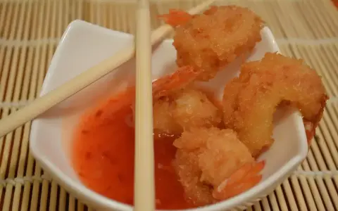 Chrupiące krewetki w panko zanurzone w słodko-kwaśnym sosie, gotowe do podania z pałeczkami.
