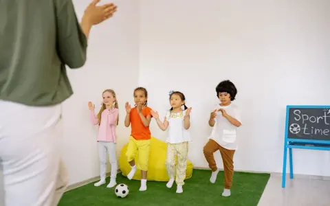Dzieci ćwiczą przy tablicy z napisem "Sport time". Krótkie hasła sportowe dla dzieci motywują do ruchu.