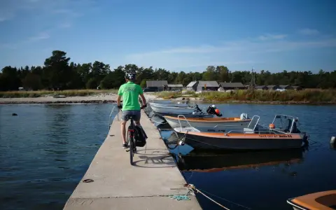 En cyklist på en brygga med båtar vid en svensk kust. Perfekt för att utforska cykelleder Sverige.