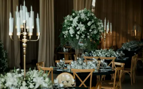 Eleganckie wesele w czarnym stylu. Stoły nakryte czarnymi obrusami, ozdobione białymi kwiatami i złotymi świecznikami.