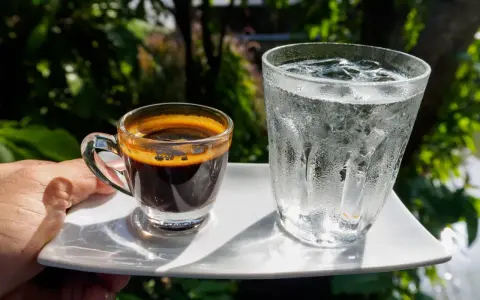 Espresso i szklanka wody z lodem na białym talerzyku. Woda do espresso przed czy po?