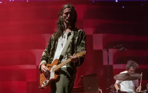 Nick Valensi spielt Gitarre auf einer Bühne, im Hintergrund ein Schlagzeuger.