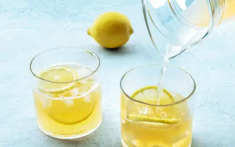 Erfrischendes zitronenwasser am morgen wird in ein Glas mit Eis und Zitronenscheiben gegossen. Eine ganze Zitrone liegt daneben.