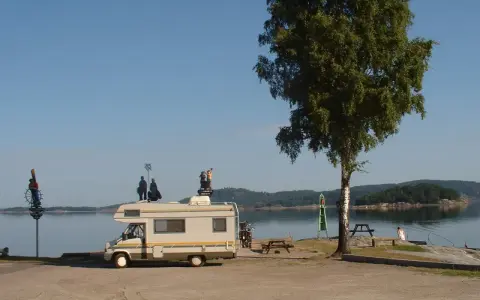 Husbil vid vattnet med figurer på taket, redo för året runt camping. En vacker plats för avkoppling.