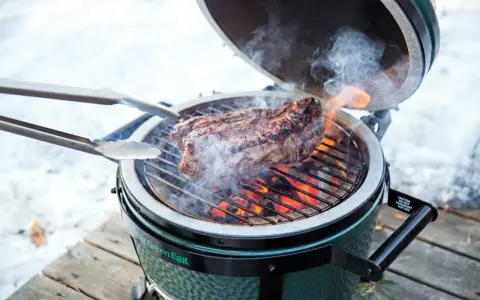 Un succulento bistec a la fiorentina cuoce sulla griglia di un Big Green Egg, circondato da fumo e fiamme.