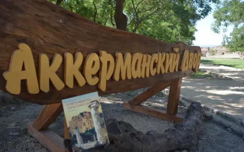 Drewniany napis "Аккерманский Двор" i książka "Sonety Krymskie" na tle stepów akermanskich i ruin.