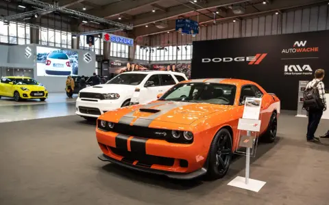 Pomarańczowy Dodge Challenger Hellcat z szarymi pasami na masce, obok białego SUV-a Dodge Durango.