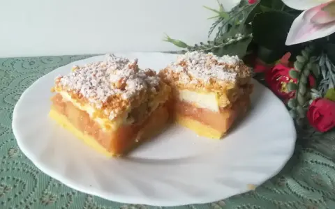 Pyszna szarlotka z bezą i kruszonką, z jabłkami i cukrem pudrem, na białym talerzu, obok kwiatów.