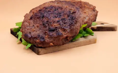 Dwa soczyste kotlety na desce, gotowe do podania. Idealne, by dowiedzieć się, jak przyprawić mięso na hamburgery.