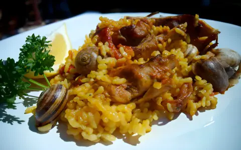 Arroz con conejo, un plato tradicional con trozos de carne dorada, arroz amarillo y caracoles, adornado con perejil y limón.