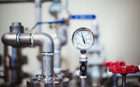 Manómetro mostrando la presión de agua en casa, rodeado de tuberías y válvulas rojas.