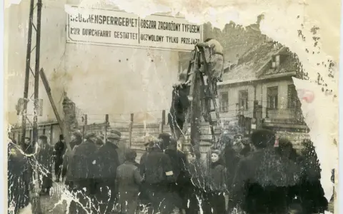 1941. Ludzie stoją przed znakiem "Obszar zagrożony tyfusem". W tle budynki i druty kolczaste.