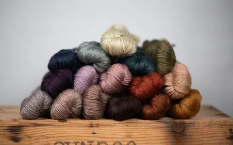 A pile of colorful yarn skeins in various earthy tones, resting on a wooden crate.