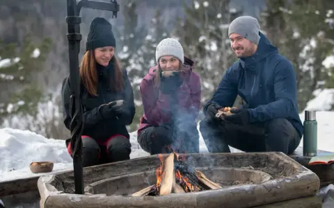 Vänner njuter av värmen från en eld och fika under härliga ute aktiviteter i snöig skogsmiljö.