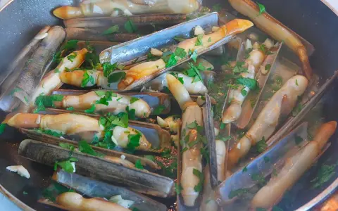 Couteaux en persillade cuits dans une poêle, parsemés de persil frais. Un plat savoureux et simple.