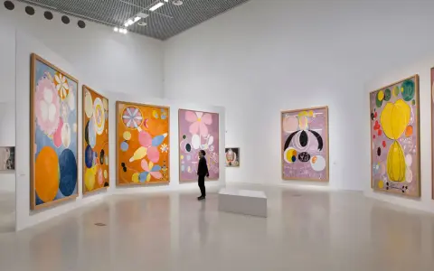 En person betraktar en samling färgstarka, abstrakta målningar av Hilma af Klint i ett ljust galleri.