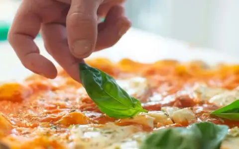Eine Hand belegt eine Pizza mit frischem Basilikum. Die Pizza belegen reihenfolge ist wichtig für den perfekten Geschmack.