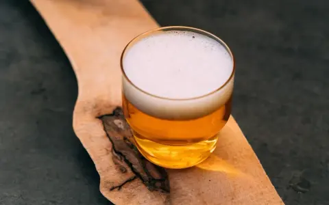 Szklanka złocistego piwa z białą pianką, prezentująca standardową dawkę alkoholu, stoi na drewnianej desce.