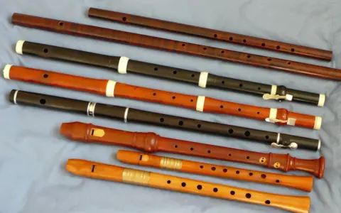 Różnorodne instrumenty renesansu, w tym flety proste o różnych rozmiarach i materiałach, ułożone na niebieskim tle.