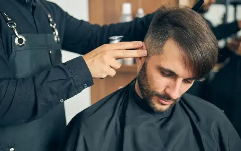Fryzjer dopracowuje męskie fryzury z grzywką do przodu, tworząc stylowy look.
