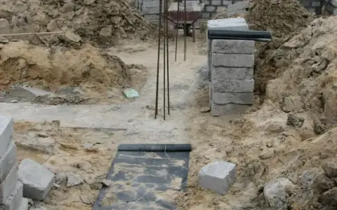 Wykonano wykopy pod fundamenty. Widać zbrojenie, betonowe bloczki i ziemię.