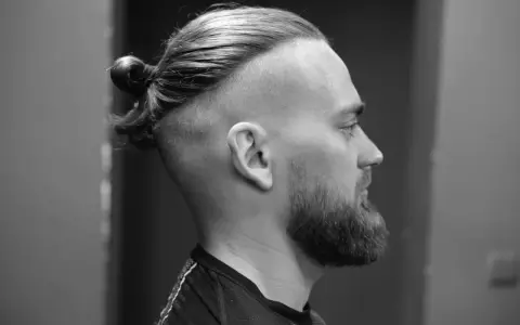 Mężczyzna z brodą i fryzurą na samuraja, z włosami upiętymi w kok na czubku głowy.
