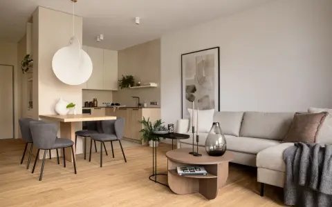 Beżowy salon inspiracje: przytulna przestrzeń z szarą sofą, drewnianym stołem i nowoczesną kuchnią.