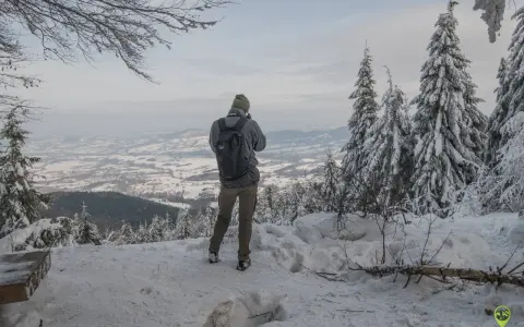Turysta podziwia zimowy krajobraz z Lubomira. Najkrótszy szlak prowadzi przez ośnieżone drzewa do punktu widokowego.