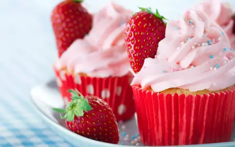 Erdbeer cupcakes mit rosa Zuckerguss und frischen Erdbeeren, verziert mit bunten Streuseln.
