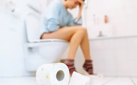 Frau sitzt auf Toilette, fühlt sich unwohl. Durchfall in der Schwangerschaft ist belastend. Toilettenpapier liegt bereit.